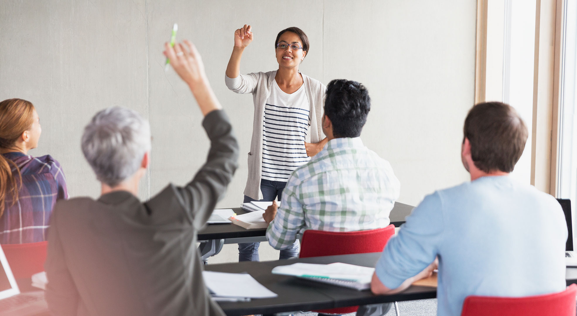A woman calling on an adult student with their handraised
