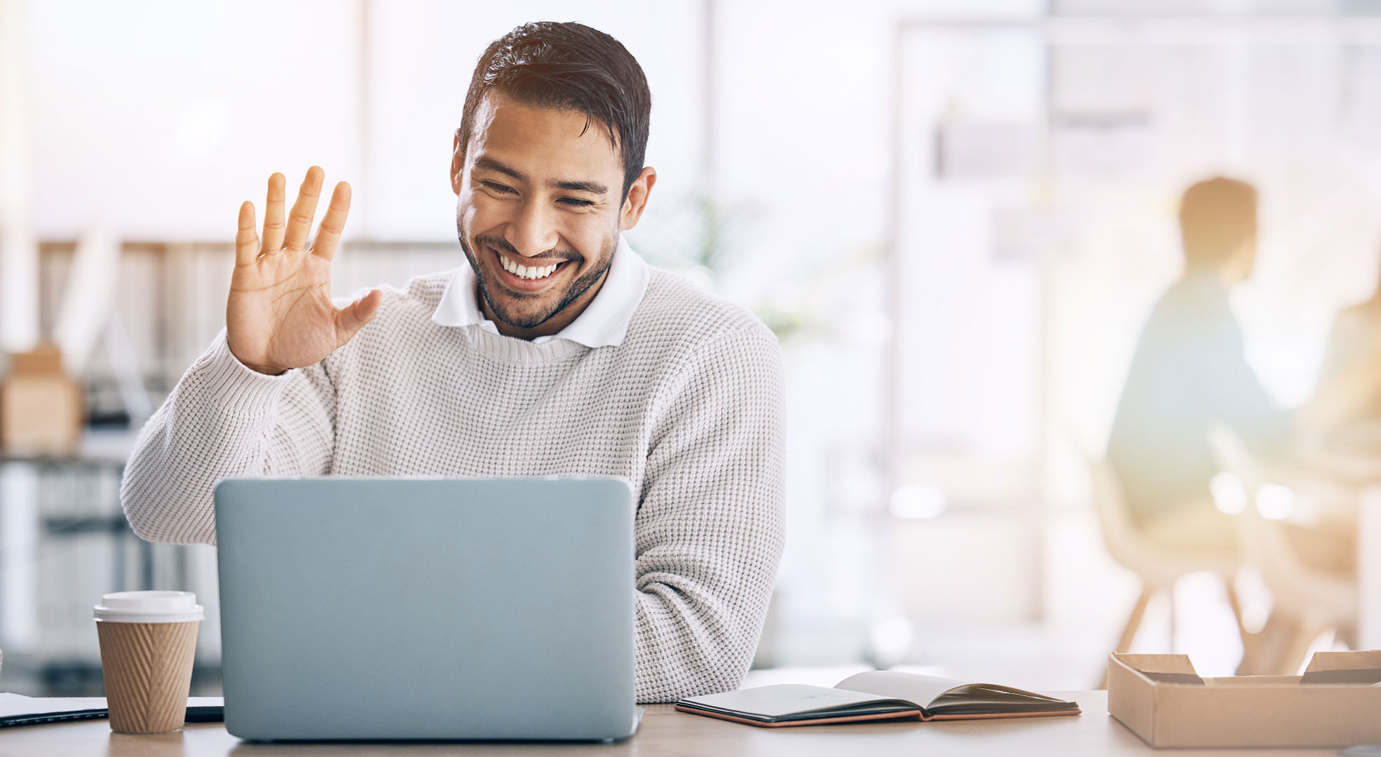 A man with coffee smiling and waving hi to a computer
